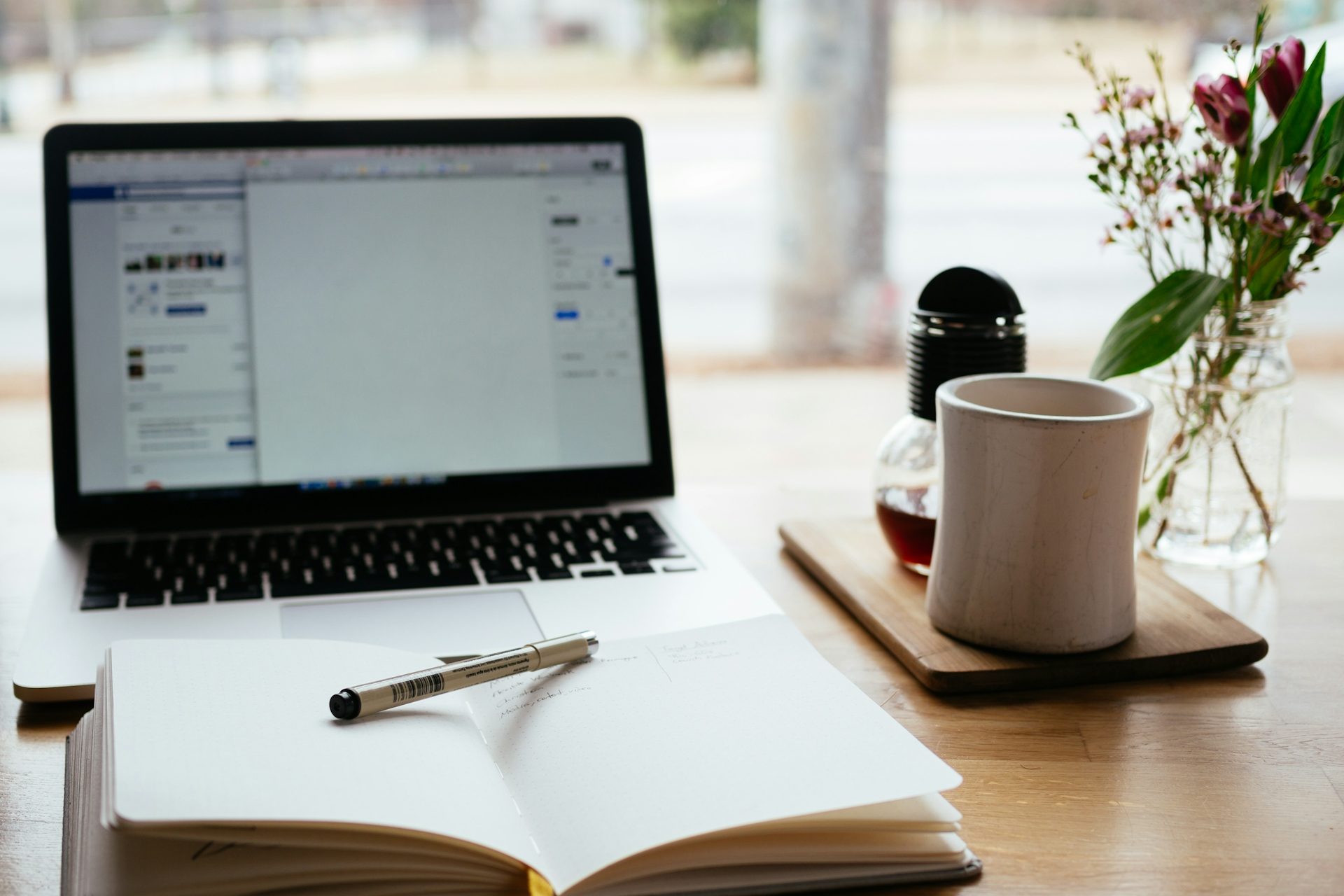die Beratung Schreibtisch mit Laptop, Notizbuch, Stift, Tasse Kaffee und frischen Blumen.